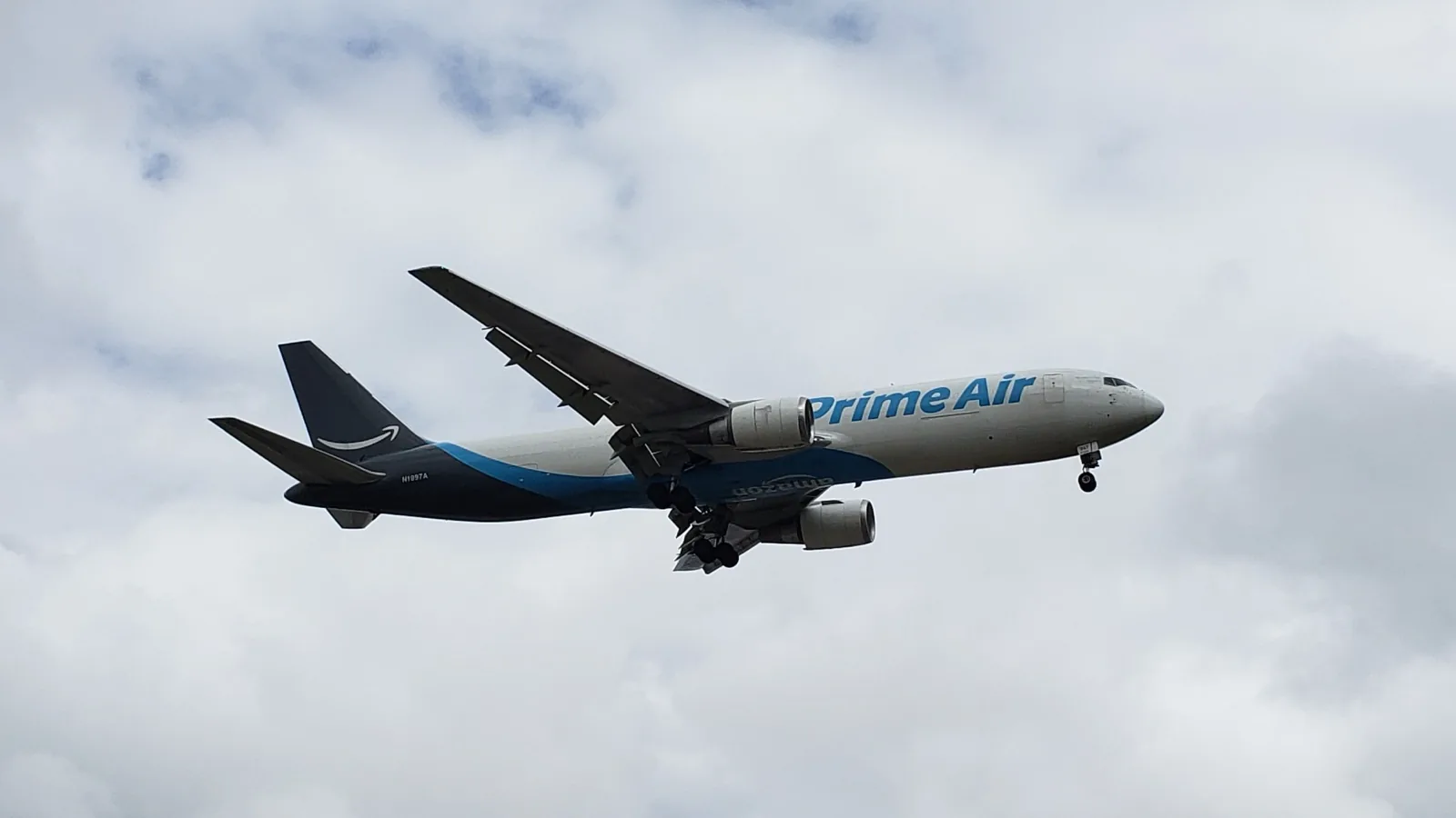 Amazon Prime Air Boeing 767-300 freighter N1997A on final approach under a gray overcast, landing gear and flaps down, the Amazon smile on its dark tail