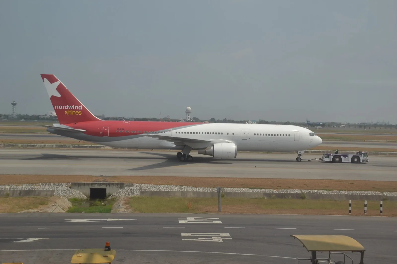 Nordwind Airlines Boeing 767 VQ-BRA, white with a red tail, being pushed by a tug across the apron at Bangkok
