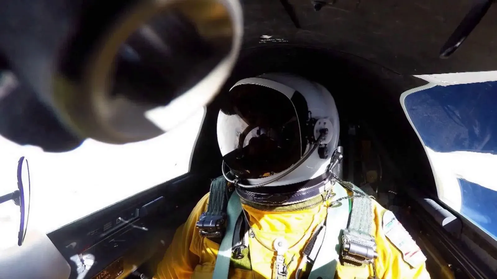 Inside the ER-2 cockpit at 65,000 feet: the pilot in a white helmet and yellow pressure suit, with a deep blue-black sky through the canopy windows