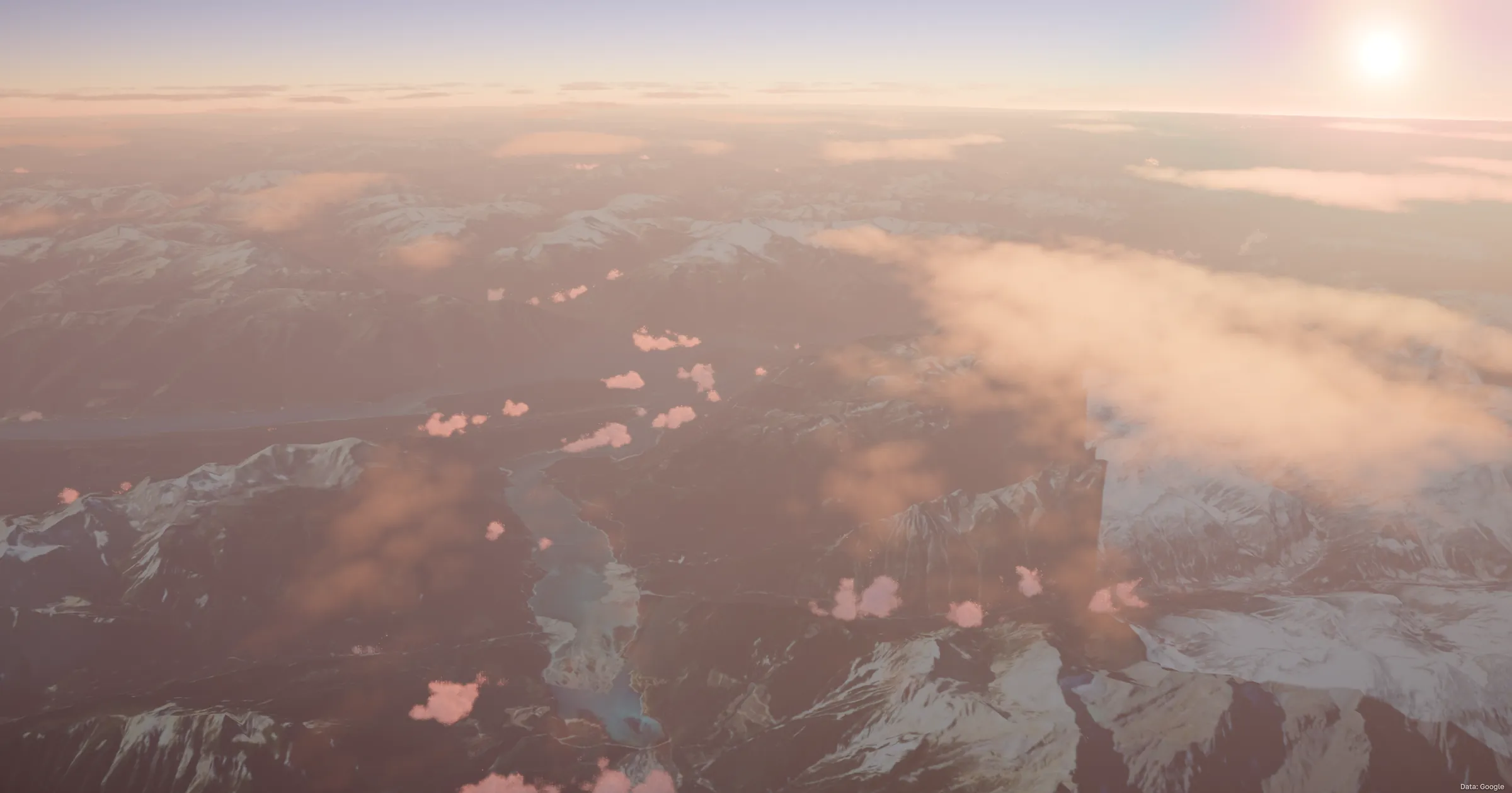 Snow-covered mountains and a river valley seen through broken cloud, with the sun bright in the upper corner