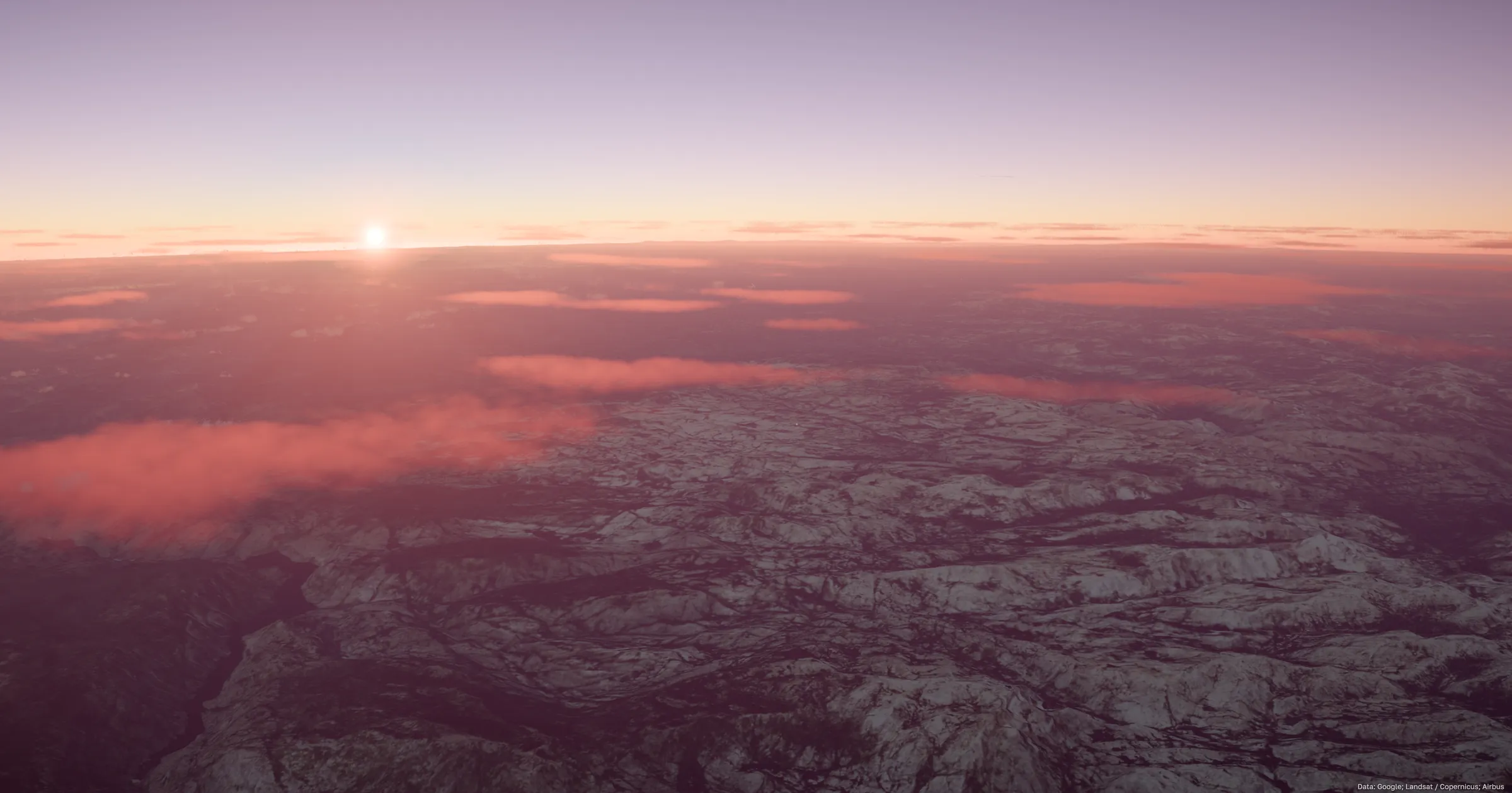 The sun sitting just above a layer of pink cloud, with snow-covered mountain ranges running to the horizon below